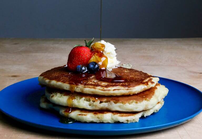 Stack of fluffy pancakes topped with syrup, strawberries, blueberries, and cream on a blue plate.