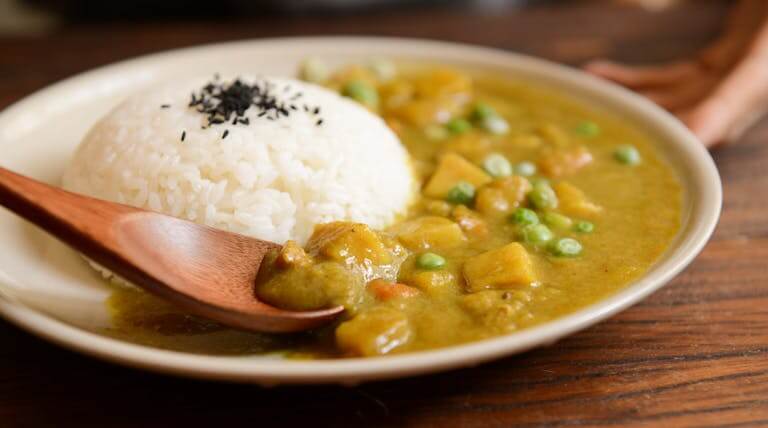 A delicious plate of creamy vegetable curry served with rice and a wooden spoon.