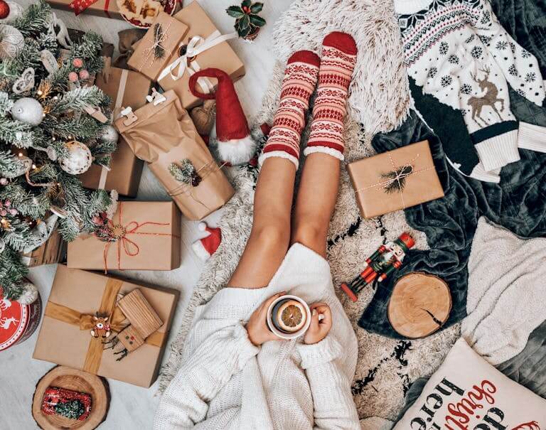 Person relaxing on Christmas morning with festive decor, gifts, and cozy mug of tea.