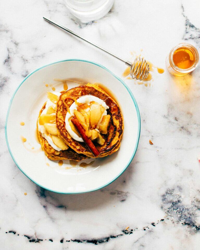 Stack of yummy pancakes with peach compote on top and honey on side.