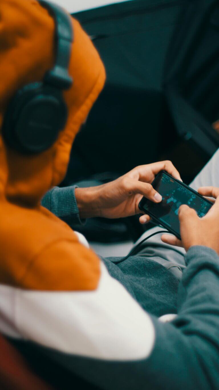 A teenager gaming on his phone while wearing headphones over his hoodie