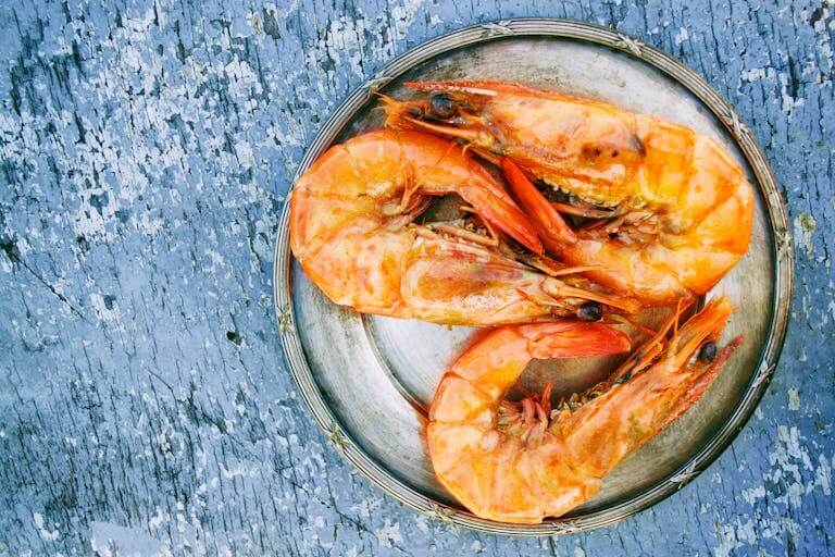 Top view of cooked shrimps on a metal plate on rustic surface.