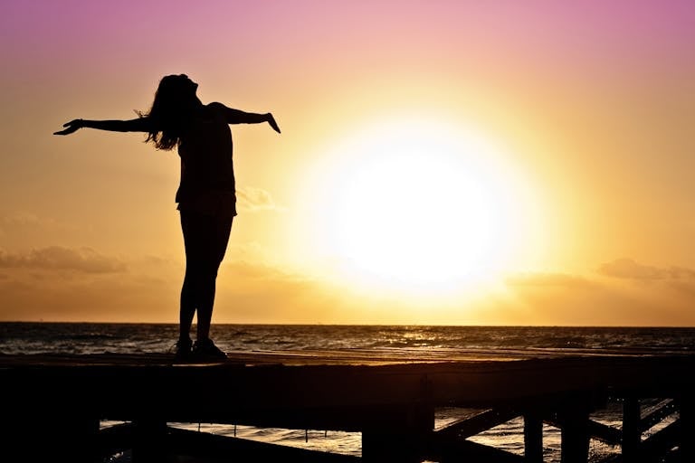 Joyful silhouette of woman standing on dock at sunset.