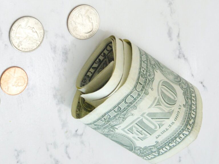 Rolled-up dollar bills and scattered coins on a marble surface, representing lifestyle creep and money management as a single parent.
