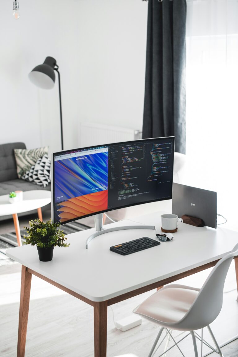 Clean white desk with widescreen monitor and closed laptop on top.