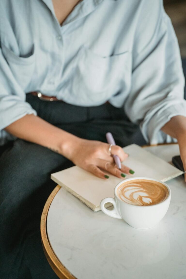 Woman writing on notebook with cup of coffee next to it