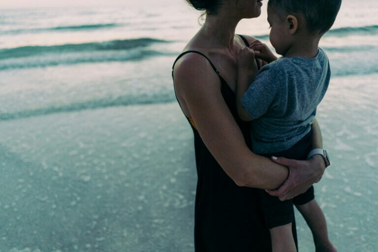 Mother carrying her young son on the beach